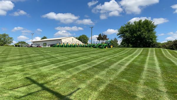 A striped lawn in front of an equipment dealership with a row of green tractors.
