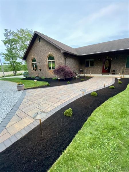 A paver walkway lined with black mulch, small shrubs, and path lights leading to a brick home.